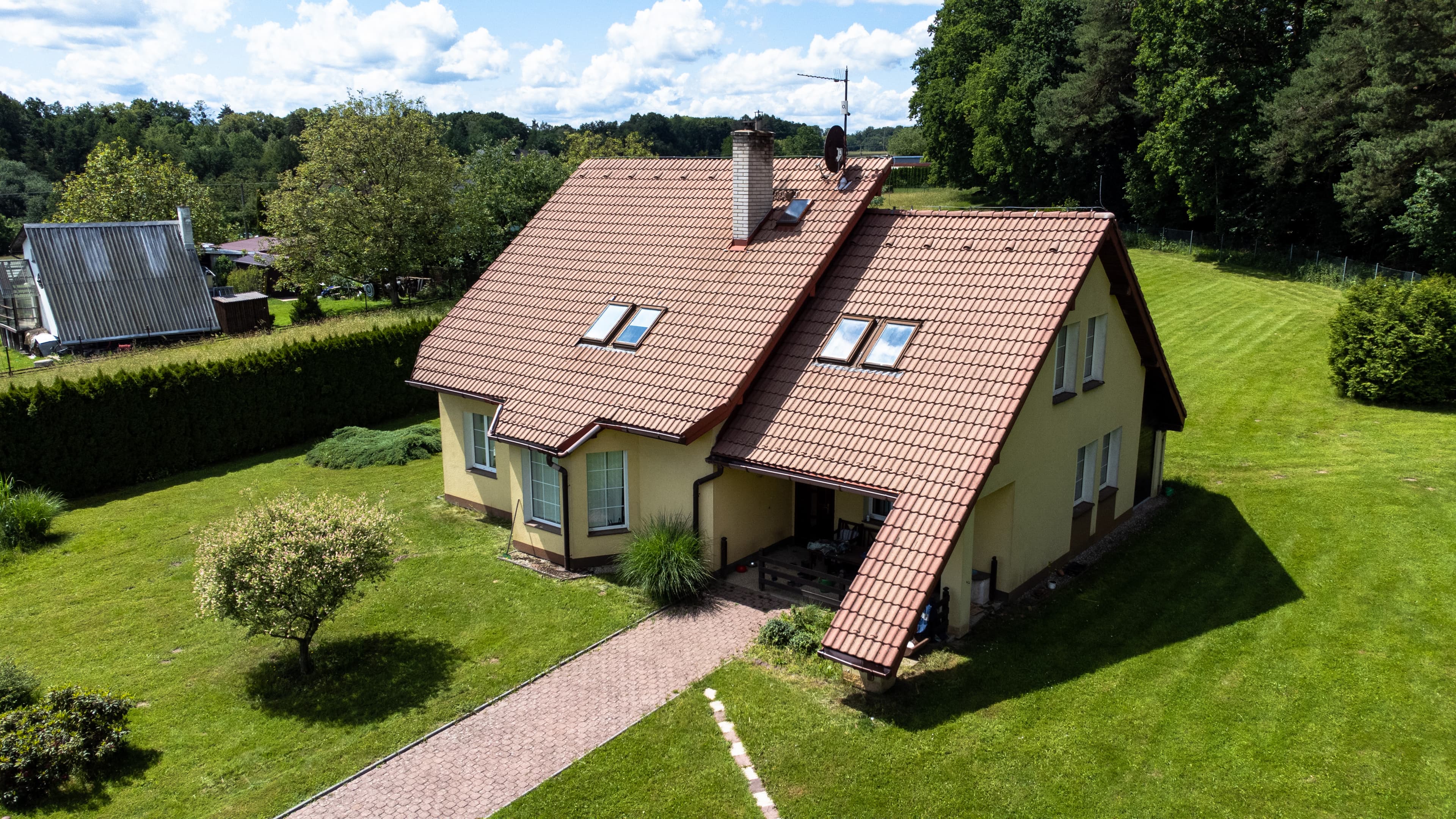 Obrázek z dronu nad rodinným domem s lesem v pozadí.