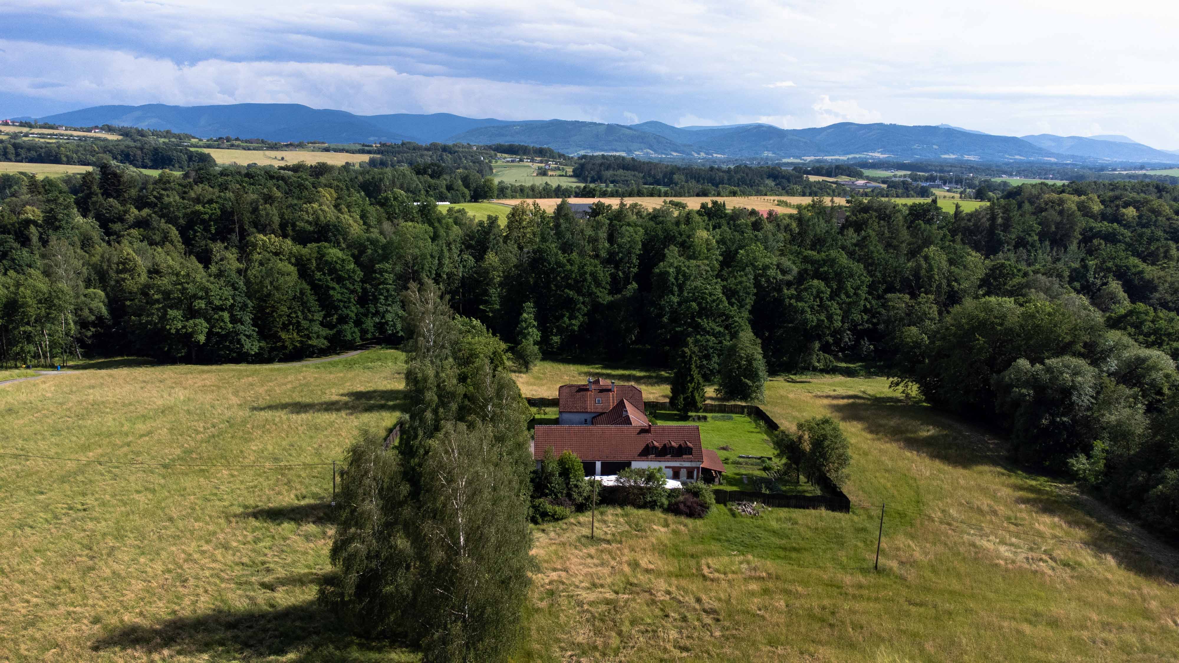 Obrázek z dronu nad rodinným domem s lesem v pozadí.