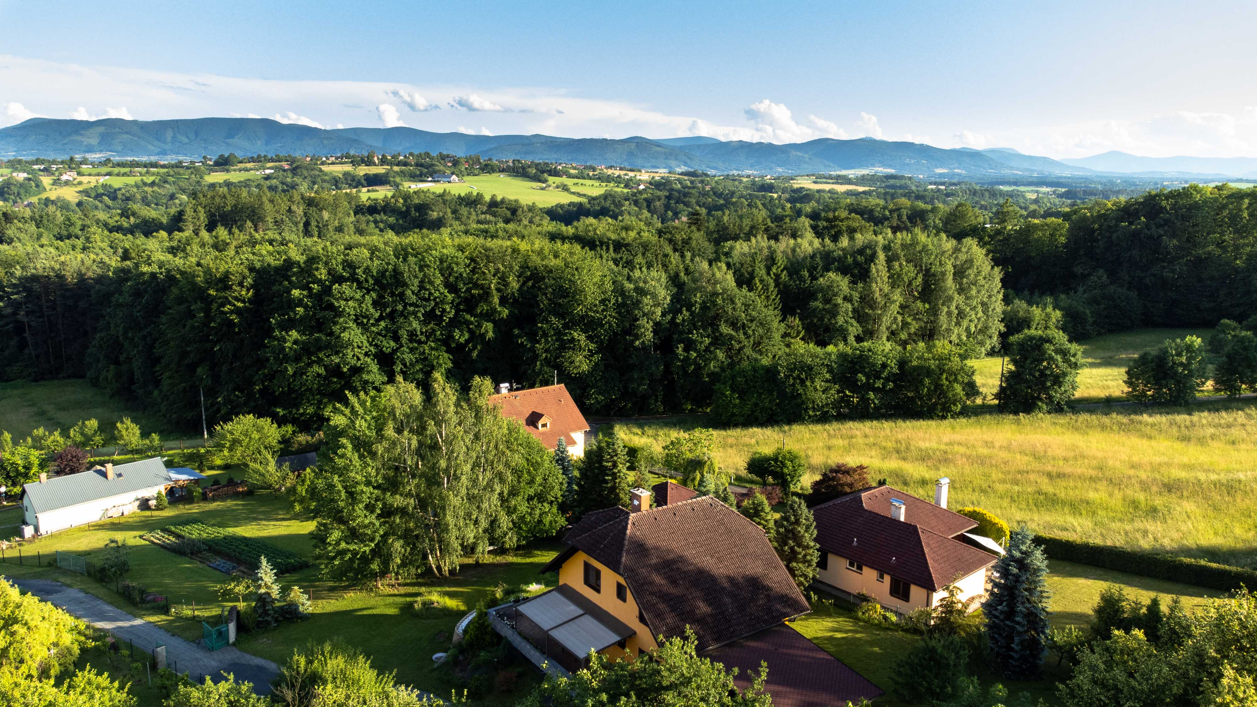 Obrázek z dronu nad rodinným domem s lesem v pozadí.