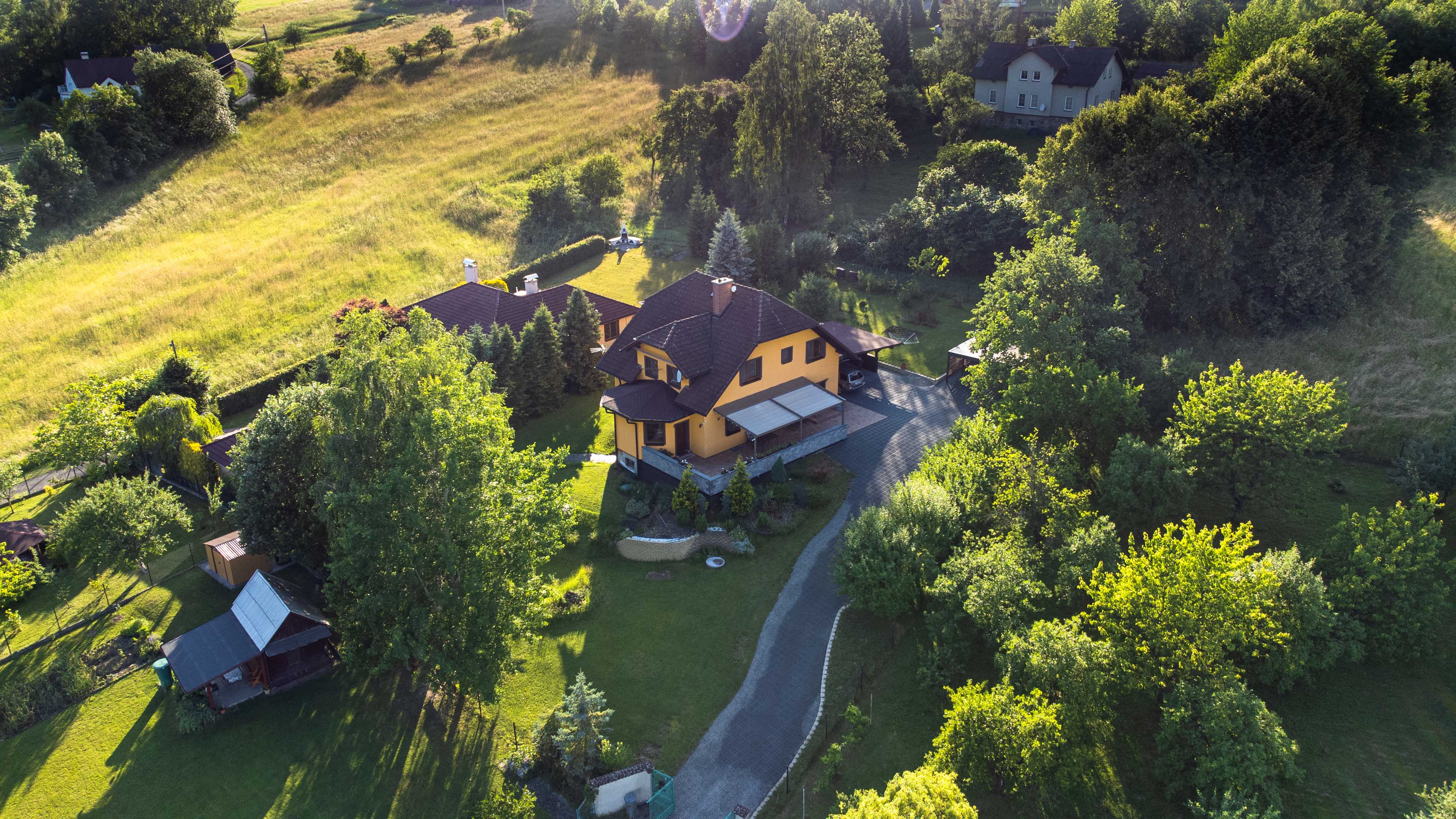 Obrázek z dronu nad rodinným domem s lesem v pozadí.